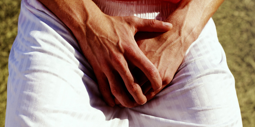 Man covering groin with hands, outdoors, close-up